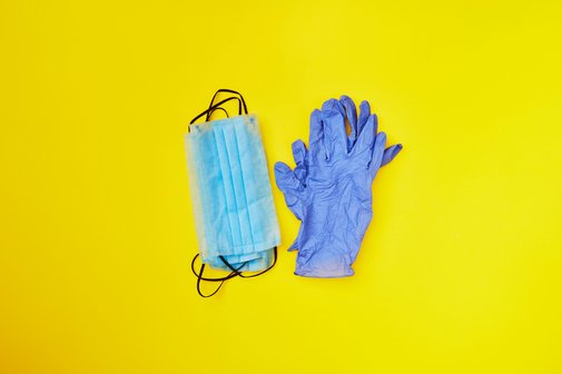 Blaue Einweg-Handschuhe und Mund-Nasen-Schutzmasken vor gelbem Hintergrund als Symbol f&uuml;r Hilfsmittel zum Verbrauch