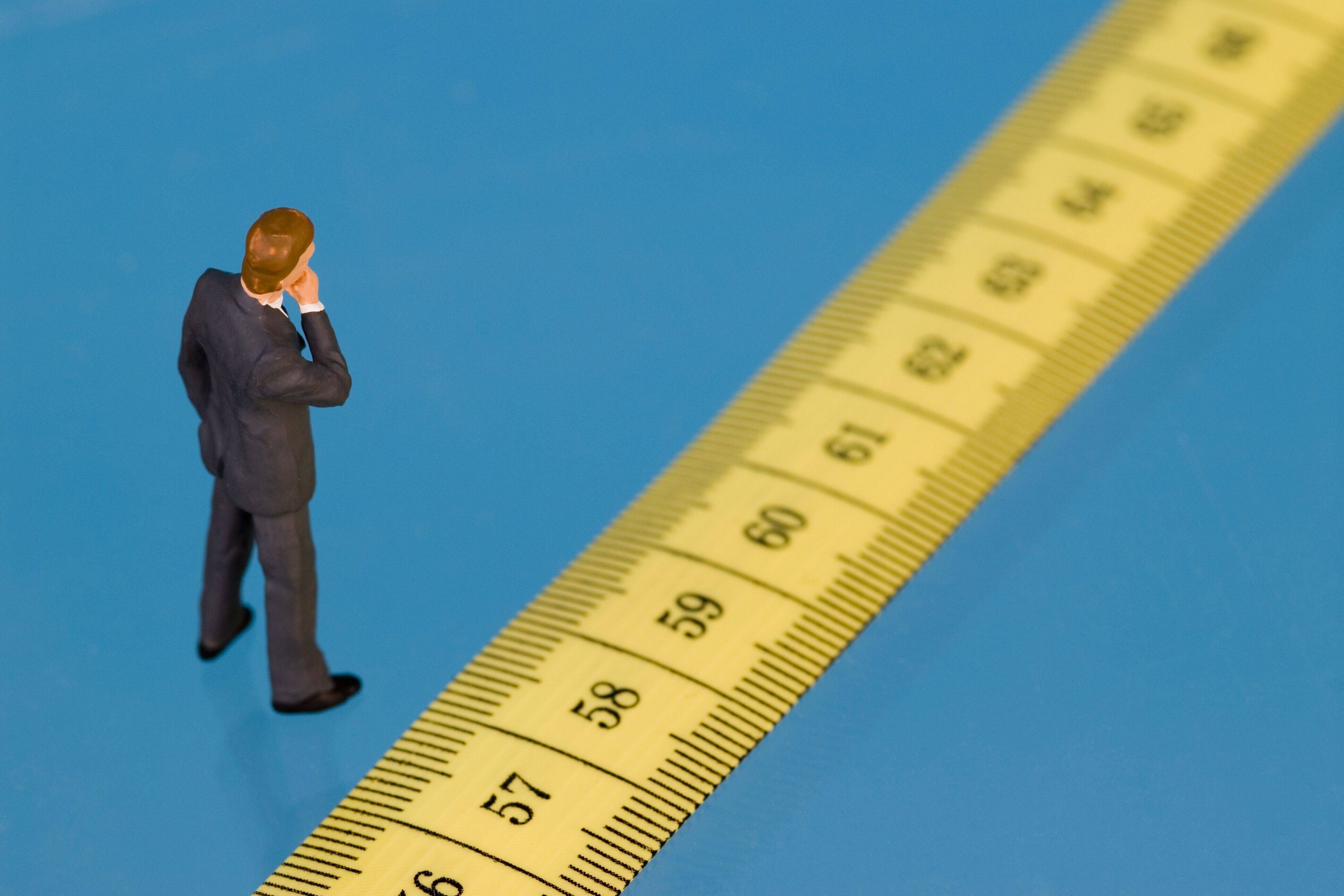 Ein Fig&uuml;rchen steht vor einem Ma&szlig;band, auf dem die Zahlen ab 57 aufw&auml;rts zu sehen sind, als Symbol f&uuml;r das Renteneintrittsalter