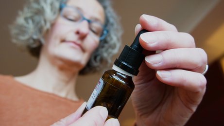 Cannabis-Therapie Das Bild zeigt Tanja Groß, die eine Medikamentenflasche mit einer Pipette zur Dosierung des Medikaments in den Händen hält.