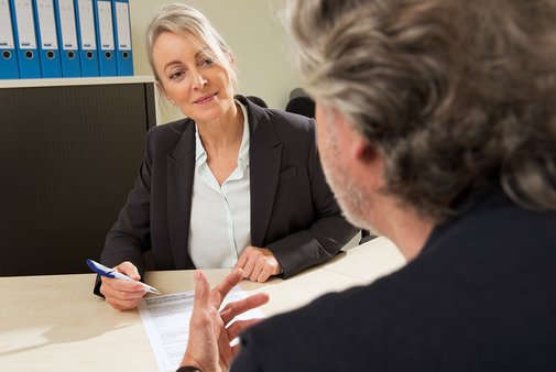 Eine Frau reicht einem Mann eine VdK-Beitrittserkl&auml;rung. Sie sitzen sich in einem B&uuml;ro gegen&uuml;ber, im Hintergrund stehen viele Aktenordner im Regal. 