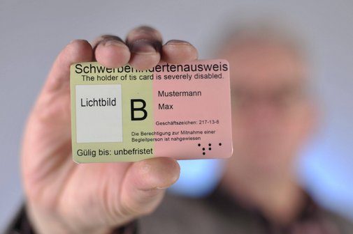 Schwerbehindertenausweis Ein Mann hält einen Schwerbehindertenausweis mit dem Merkzeichen B in die Kamera.