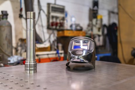 Schweißer erleidet Kehlkopfkrebs, Anerkennung als Berufskrankheit Ein Schweißerhelm auf einem menschenleeren Tisch in einer Fabrik.