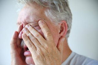 Ein Mann fasst sich mit beiden Händen ins Gesicht und an die Nase, er guckt leidend, hat die Augen geschlossen. 