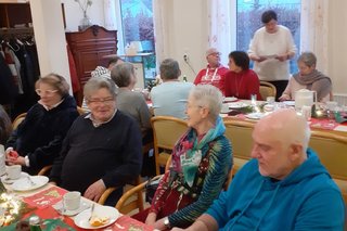 Personen am gedeckten Tisch, mit Kaffee und Gebäck, sich angeregt unterhaltend