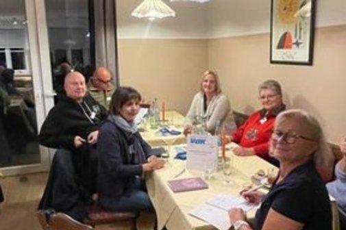 Ein paar Teilnehmer sitzen am Tisch und l&auml;cheln in die Kamera