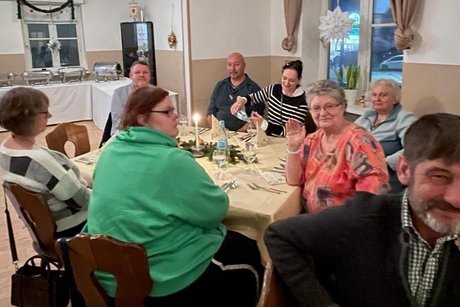 Einige Teilnehmer am Tisch. Eine Dame winkt fr&ouml;hlich in die Kamera