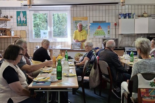 Dem Käsegenuss auf der Spur An Tischen sitzen die Teilnehmer der Käseverkostung und vorne steht der Vortragende