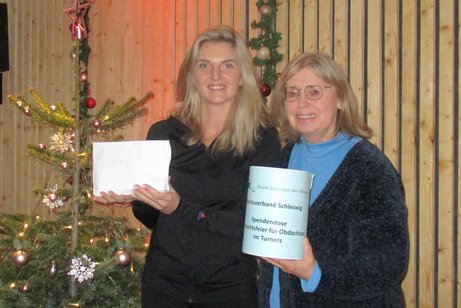 2 Personen, die eine Spendendose in der Hand halten, deren Summe von 347,70 € an Obdachlose gehen