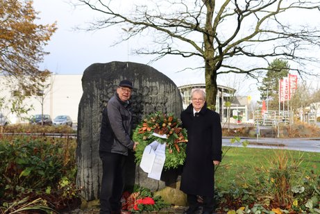 2 Personen stehen mit einem Kranz vor einem Ehrenmal