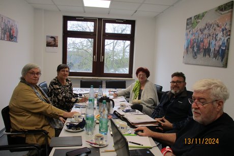 5 Personen, Vorstand und Gäste, sitzen um einen großen Tisch und beraten die Aufgaben