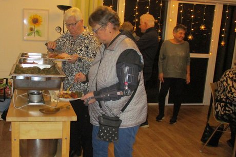 Personen an einem Buffet, nehmen sich Speisen (Grünkohl) auf Ihre Teller