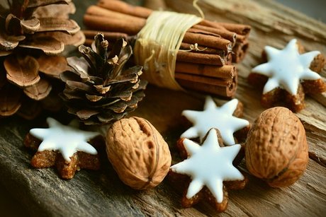 auf einem Holztisch liegen weihnachtlich geschmückt Tannenzapfen, Sternenkekse mit Zuckerglasur und Zimtstangen