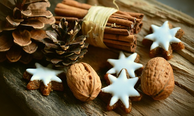 auf einem Holztisch liegen weihnachtlich geschmückt Tannenzapfen, Sternenkekse mit Zuckerglasur und Zimtstangen